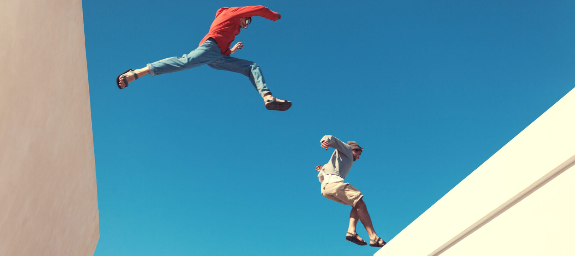 2 people jumping across a gap between buildings